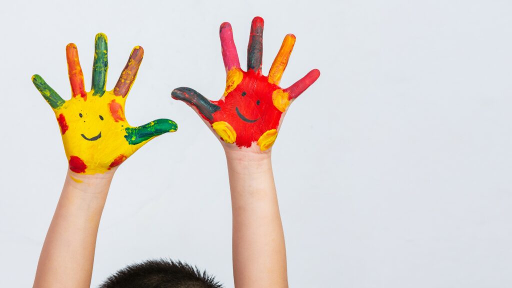 Enfant qui lève les mains en l'air avec de la peinture pour montrer le service de garde d'enfant proposé par Tyché Company services.